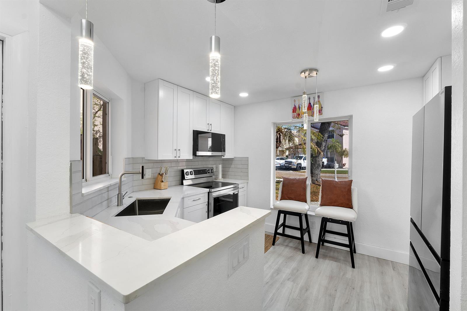 A modern kitchen features white cabinets, quartz countertops, stainless steel appliances, and a breakfast bar — 6363 Seagrape Circle, Margate FL 33063, MARGATE, FL
