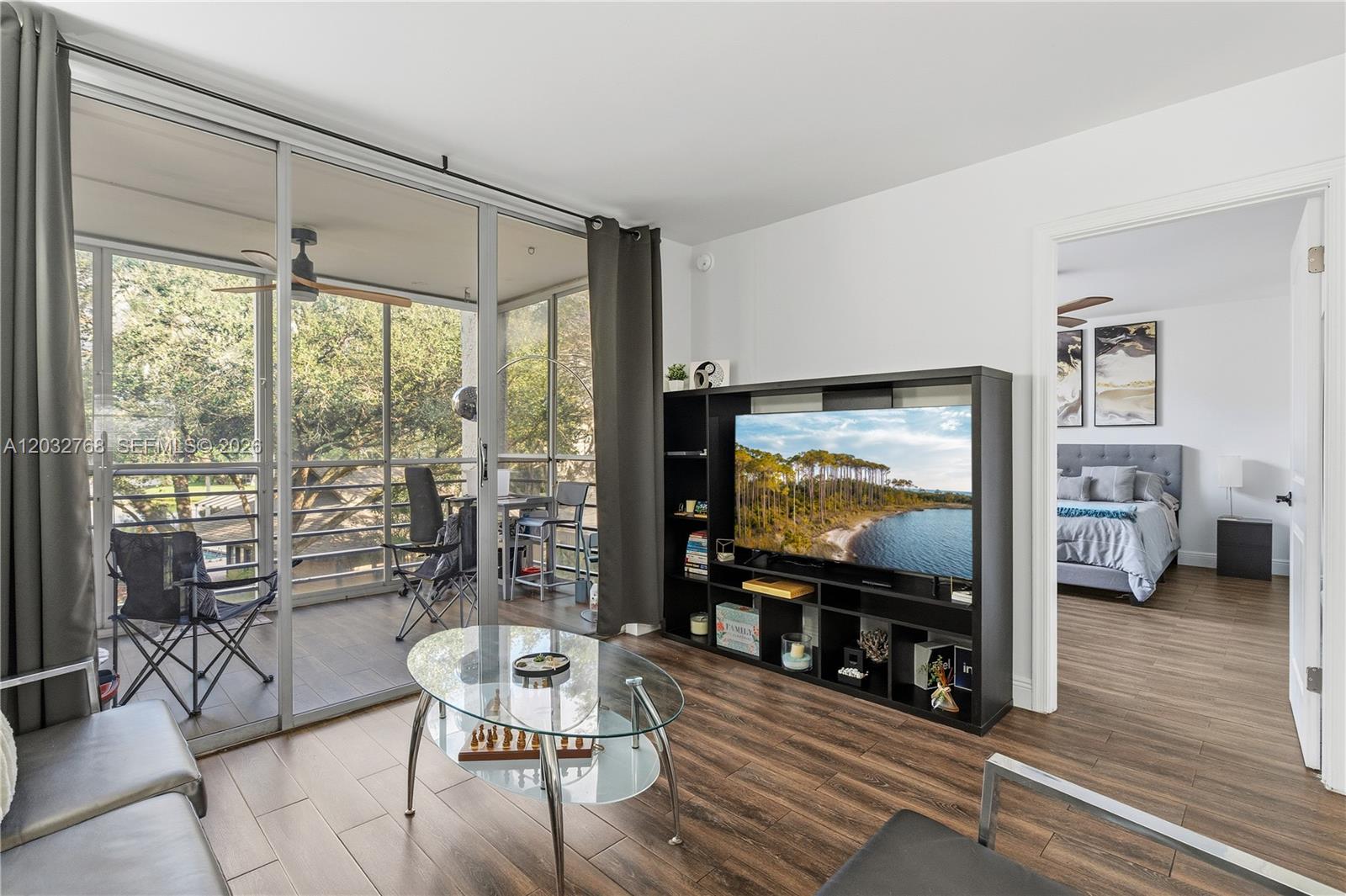 A living room features wood-look flooring, a black media console, and a screened-in balcony — 9340 Lagoon Pl # 304, Davie FL 33324, DAVIE, FL
