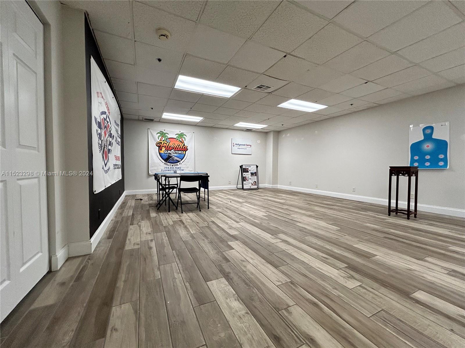 A room with wood-look flooring, a drop ceiling, and a target poster on the wall — 2055 Liberty St, Hollywood FL 33020, HOLLYWOOD, FL