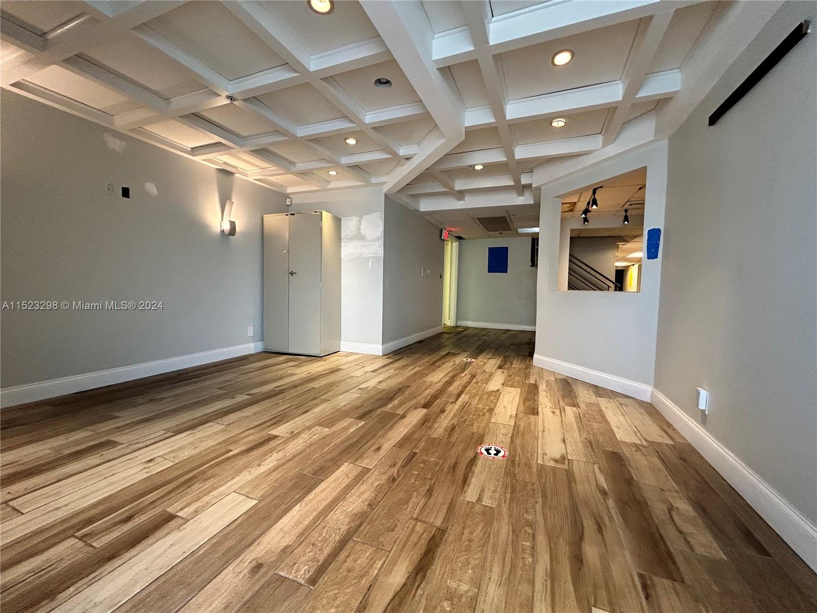 An empty room features wood-look flooring, a coffered ceiling with recessed lighting, and a storage cabinet — 2055 Liberty St, Hollywood FL 33020, HOLLYWOOD, FL
