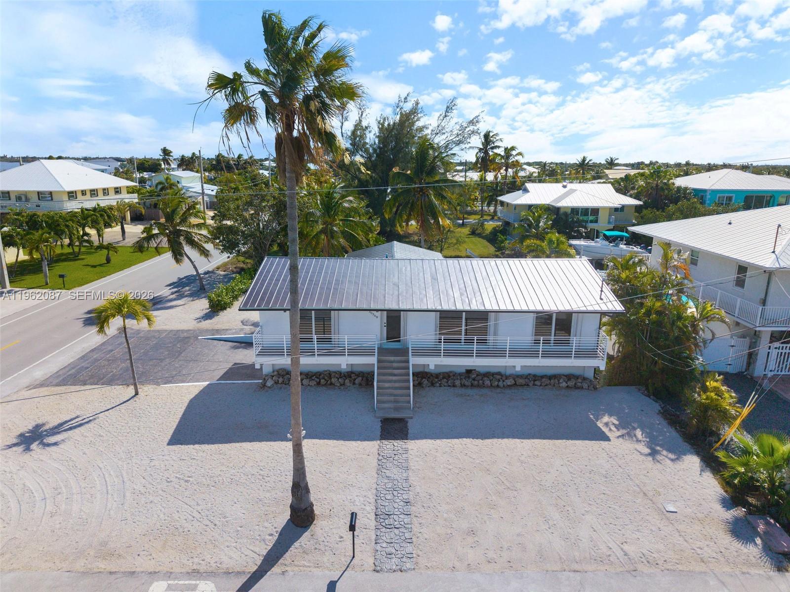 An elevated white house with a metal roof sits on a sandy lot with palms — 30368 Killdeer Ln, Big Pine FL 33043, BIG PINE, FL