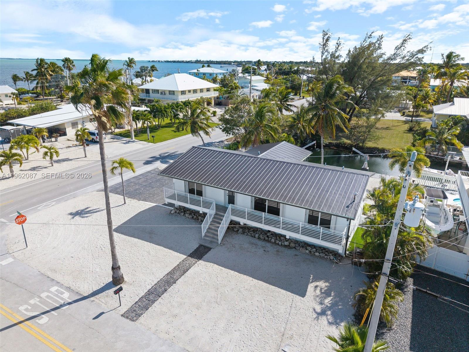 An elevated white house with a dark metal roof sits near a canal and road — 30368 Killdeer Ln, Big Pine FL 33043, BIG PINE, FL
