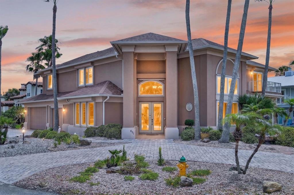 A two-story tan house with a paved driveway and palm trees at sunset — 621 RIVER VIEW ROAD, FLAGLER BEACH, FL