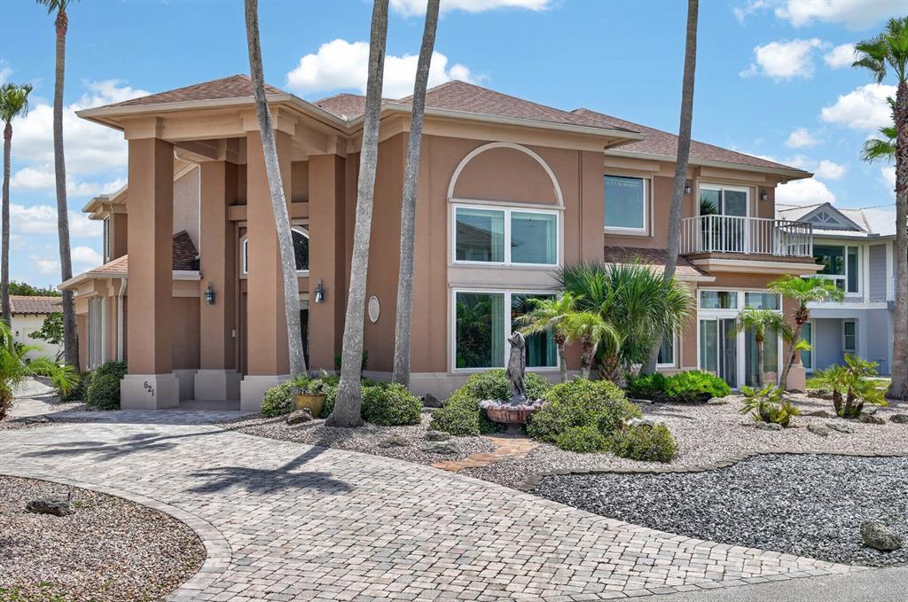 A two-story tan stucco house with a paved driveway, palm trees, and a front fountain — 621 RIVER VIEW ROAD, FLAGLER BEACH, FL