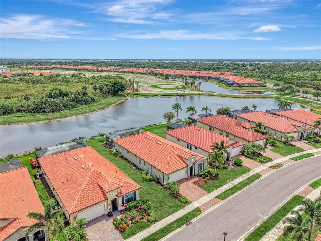An aerial view of suburban houses with orange tile roofs bordering a lake and golf course — 24268 GALLBERRY DRIVE, VENICE, FL