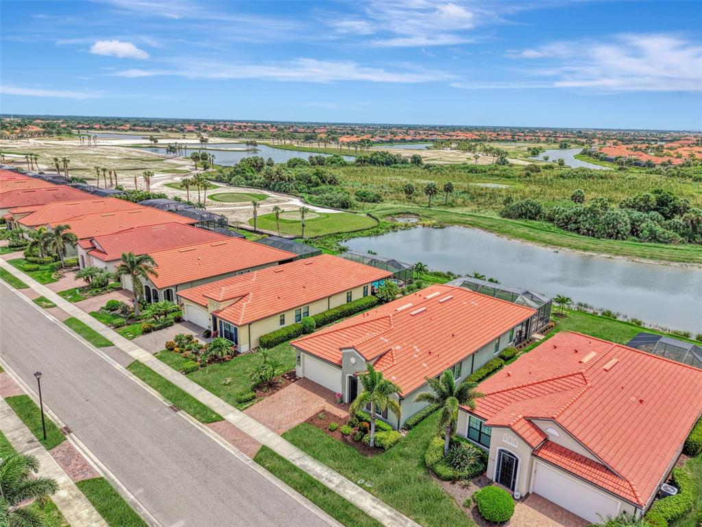 An aerial view shows a row of houses with orange tile roofs near a lake — 24268 GALLBERRY DRIVE, VENICE, FL