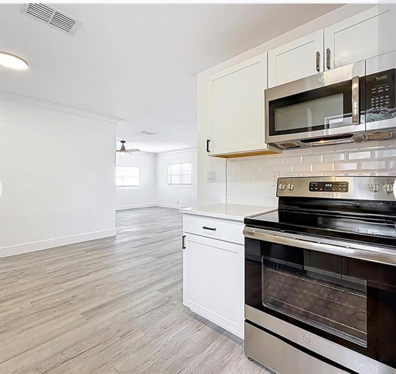 A kitchen with white cabinets, stainless steel appliances, a subway tile backsplash, and wood-look flooring — 200 LEWIS BOULEVARD SE, ST PETERSBURG, FL