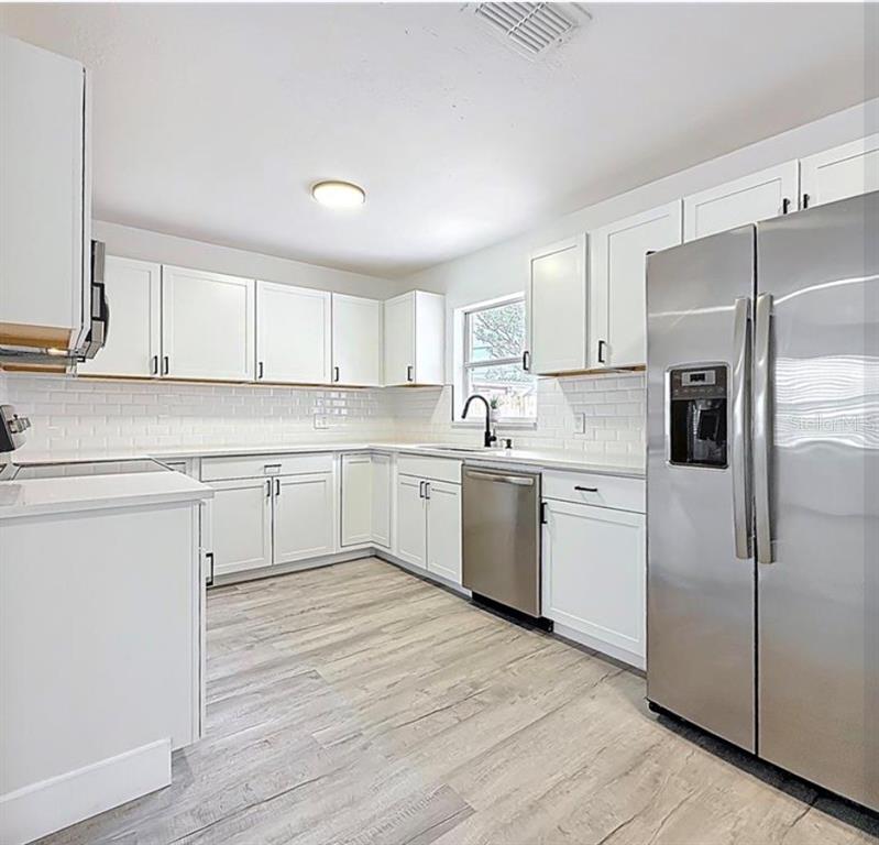 A kitchen features white cabinets, stainless steel appliances, a subway tile backsplash, and light flooring — 200 LEWIS BOULEVARD SE, ST PETERSBURG, FL