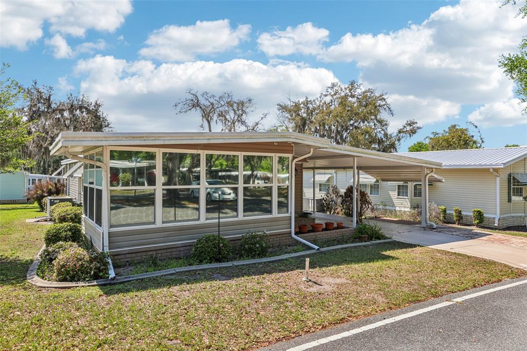 A single-story mobile home with a large glass-enclosed sunroom and an attached carport — 105 ORCHID WAY, LEESBURG, FL