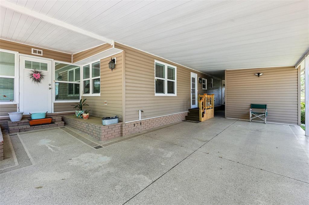 A tan mobile home exterior features a large concrete carport and a brick-trimmed front porch — 105 ORCHID WAY, LEESBURG, FL