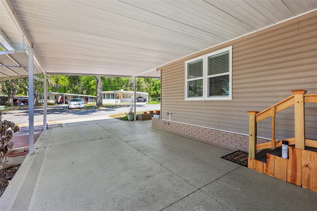 A concrete carport area features a tan-sided exterior wall with a window and wooden stairs — 105 ORCHID WAY, LEESBURG, FL