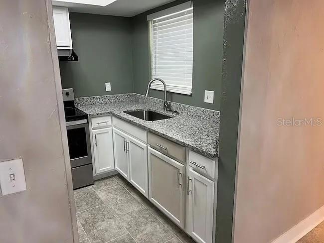 A kitchen features white cabinets, granite countertops, a stainless steel stove, and dark green walls — 23104 SANDALWOOD DRIVE UNIT 104, WILDWOOD, FL