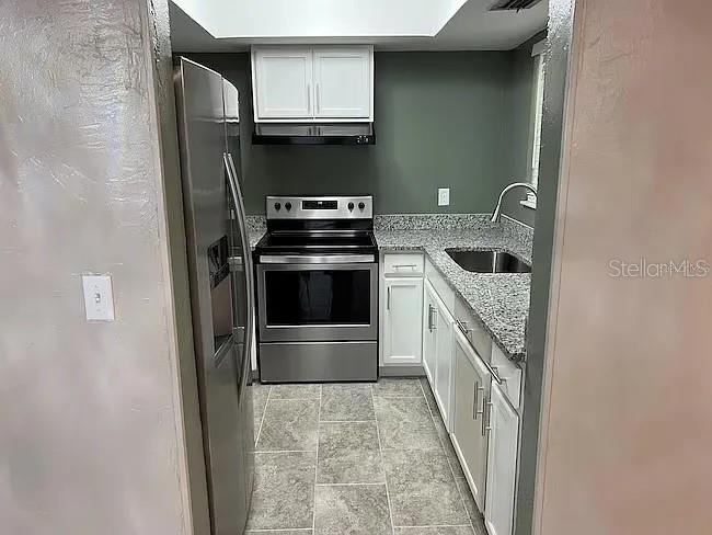 A galley kitchen features stainless steel appliances, white cabinets, and granite countertops — 23104 SANDALWOOD DRIVE UNIT 104, WILDWOOD, FL