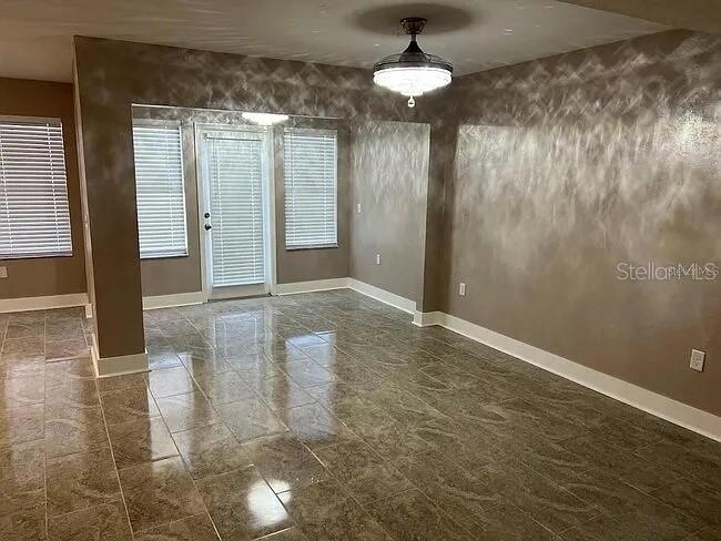 An empty room features glossy tile flooring, textured gray walls, and a central ceiling fan — 23104 SANDALWOOD DRIVE UNIT 104, WILDWOOD, FL
