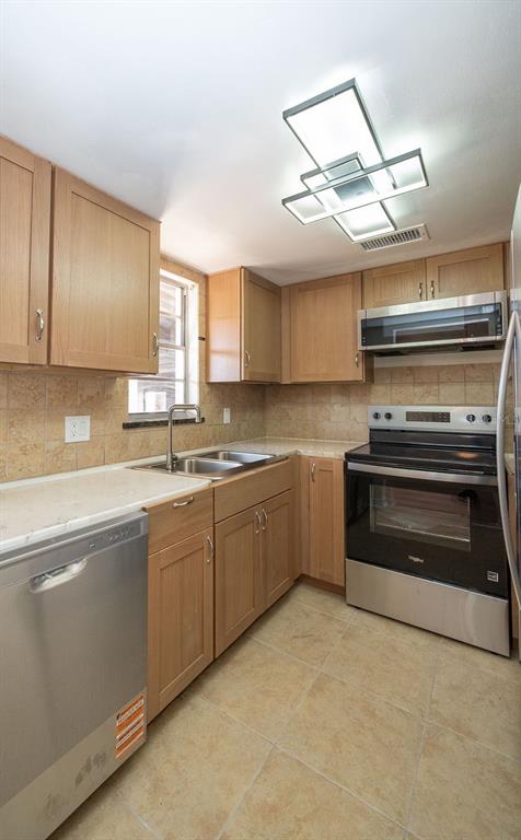 A kitchen with light wood cabinets, stainless steel appliances, and tan tile flooring — 4807 MARINE PARKWAY UNIT 103, NEW PORT RICHEY, FL