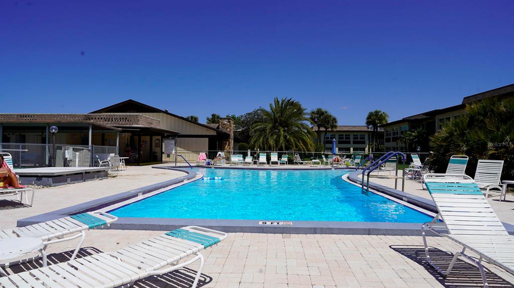 An outdoor swimming pool surrounded by lounge chairs and apartment buildings under a clear sky — 4807 MARINE PARKWAY UNIT 103, NEW PORT RICHEY, FL