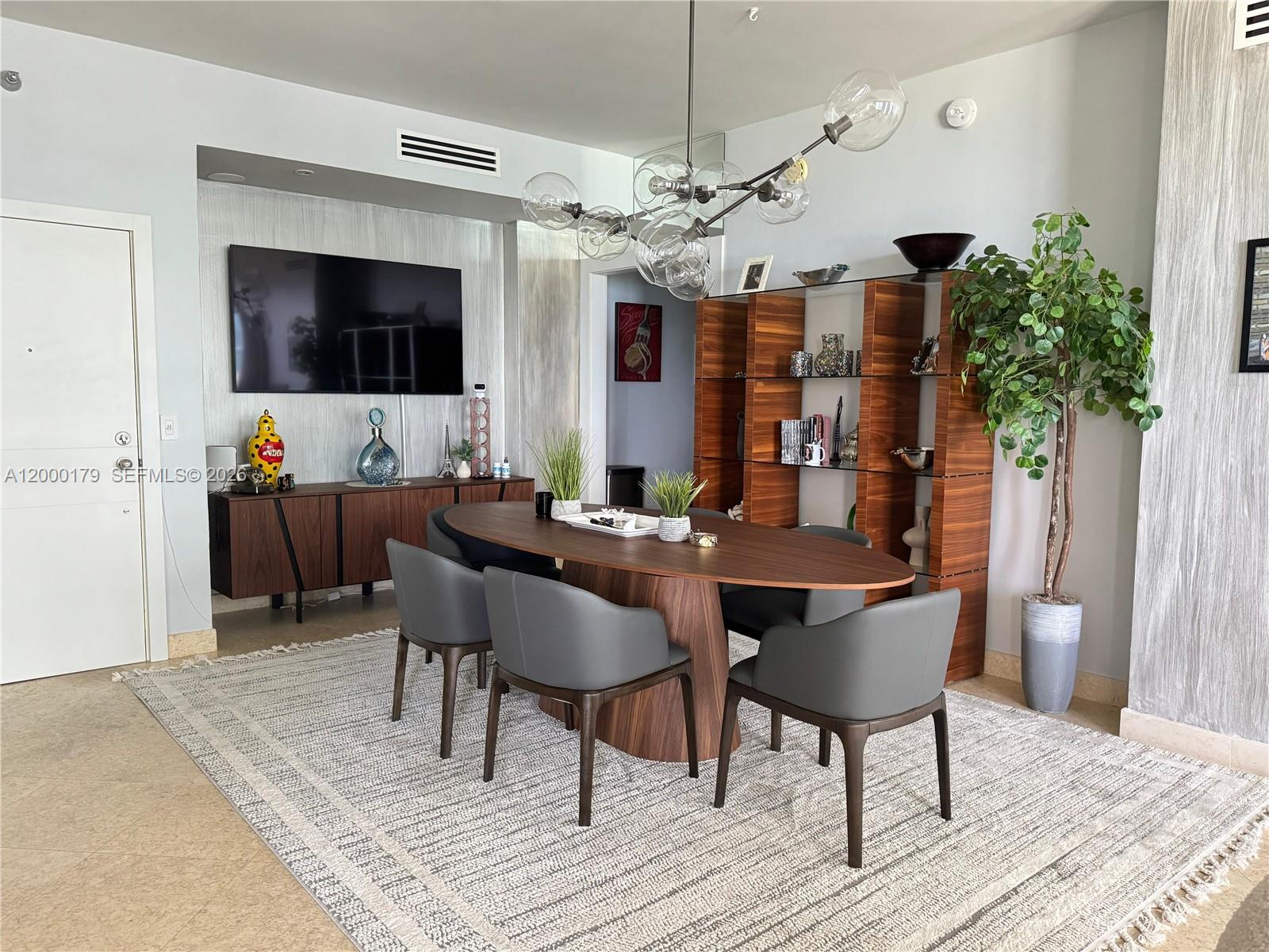 A dining area features an oval wooden table, gray chairs, and a modern glass chandelier — 10185 collins # 20, Bal Harbour FL 33154, BAL HARBOUR, FL