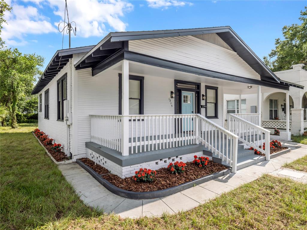A white house with dark trim, a front porch, and red flowers in the landscaping — 1215 E 26TH AVENUE, TAMPA, FL