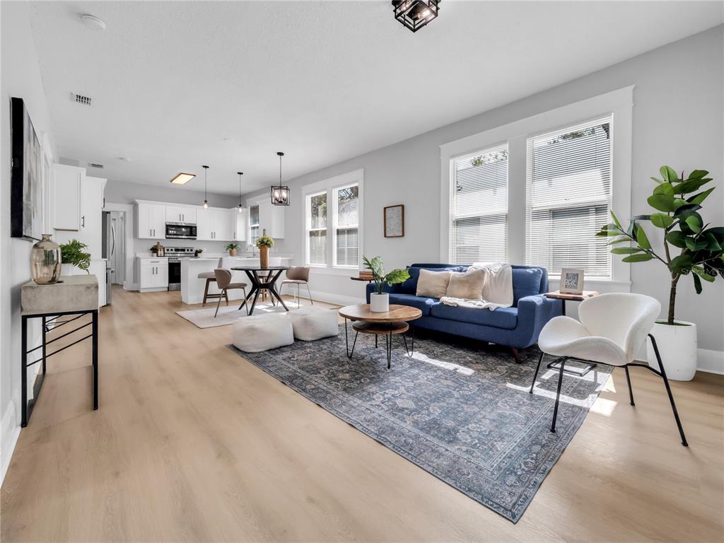 An open-concept living room and kitchen featuring light wood floors, a blue sofa, and white cabinetry — 1215 E 26TH AVENUE, TAMPA, FL