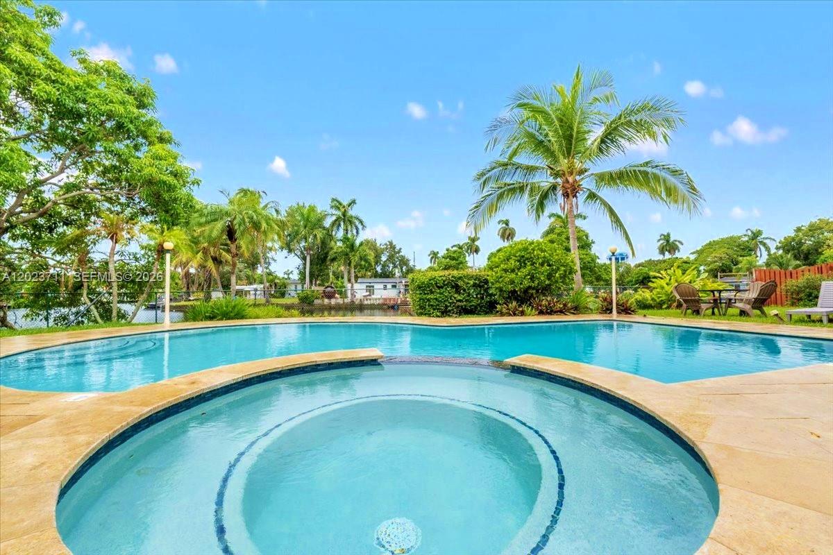A circular hot tub sits in the foreground of a swimming pool with palm trees — 2650 Scott St, Hollywood FL 33020, HOLLYWOOD, FL
