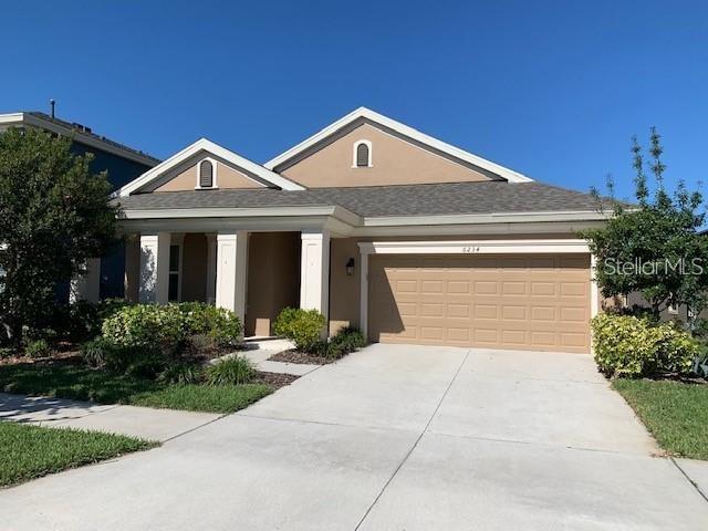 A single-story suburban house features a tan stucco exterior, a two-car garage, and a driveway — 6234 COLMAR PLACE, APOLLO BEACH, FL