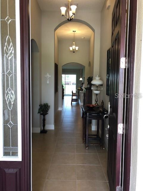 A view from an entryway into a tiled hallway with arched doorways and hanging chandeliers — 6234 COLMAR PLACE, APOLLO BEACH, FL