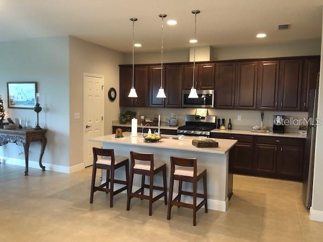 A kitchen features dark wood cabinets, a central island with three stools, and pendant lighting — 6234 COLMAR PLACE, APOLLO BEACH, FL