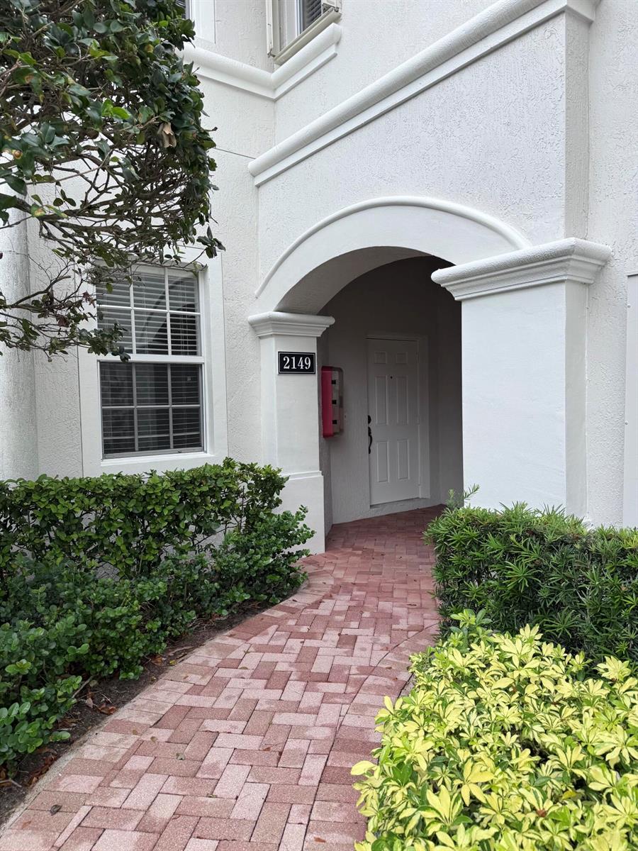 A brick walkway leads to the arched entryway of a white building with unit number 2149 — 2149 Wingate Bend, Wellington FL 33414, WELLINGTON, FL
