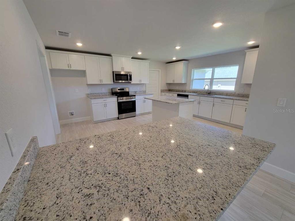 A kitchen features white cabinets, granite countertops, a central island, and stainless steel appliances — 8247 SW 125TH COURT ROAD, DUNNELLON, FL