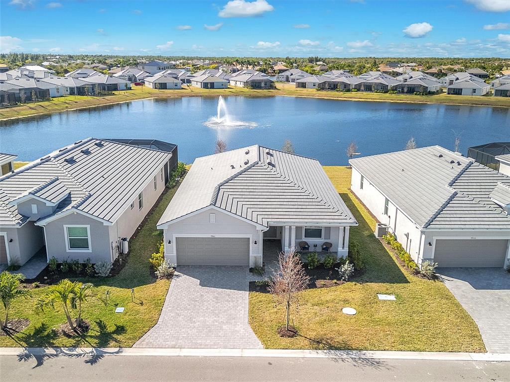 An aerial view shows three suburban houses with gray roofs facing a central pond — 7961 LAKES EDGE LANE, PORT CHARLOTTE, FL