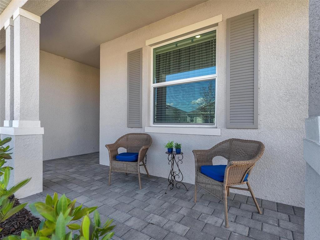 A covered front porch features two wicker chairs with blue cushions and a small table — 7961 LAKES EDGE LANE, PORT CHARLOTTE, FL