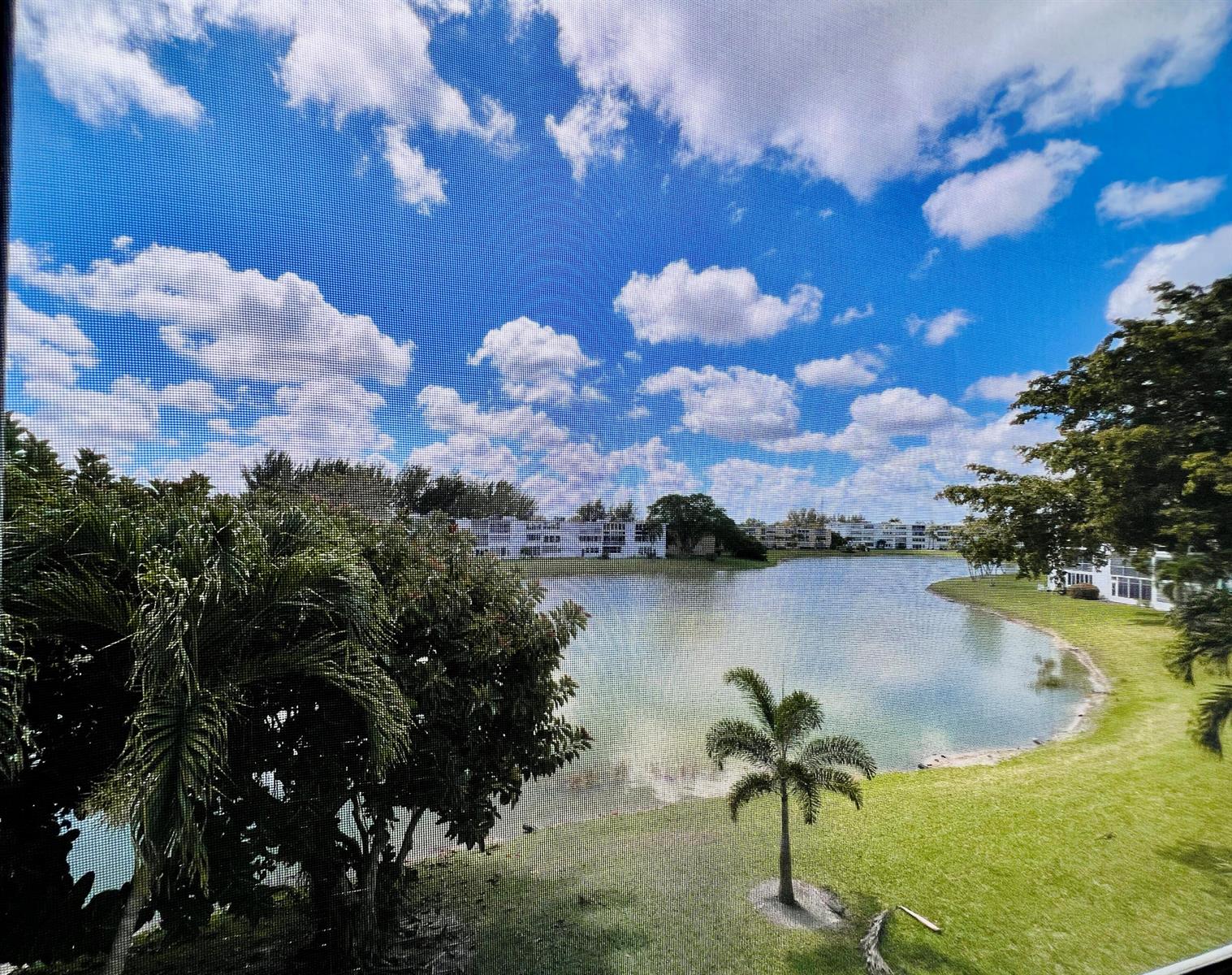 A view of a lake and apartment buildings seen through a window screen — 314 Wellington D, West Palm Beach FL 33417, WEST PALM BEACH, FL