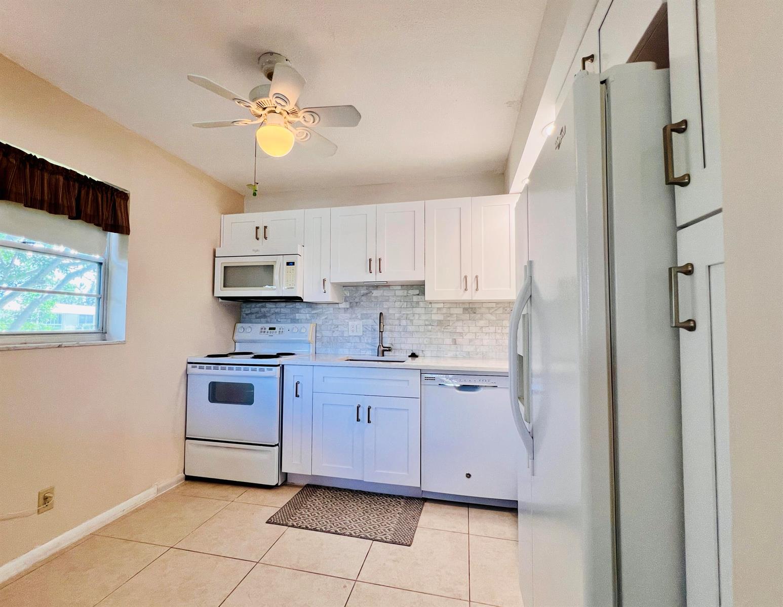 A kitchen features white cabinets, white appliances, a tiled backsplash, and a ceiling fan — 314 Wellington D, West Palm Beach FL 33417, WEST PALM BEACH, FL