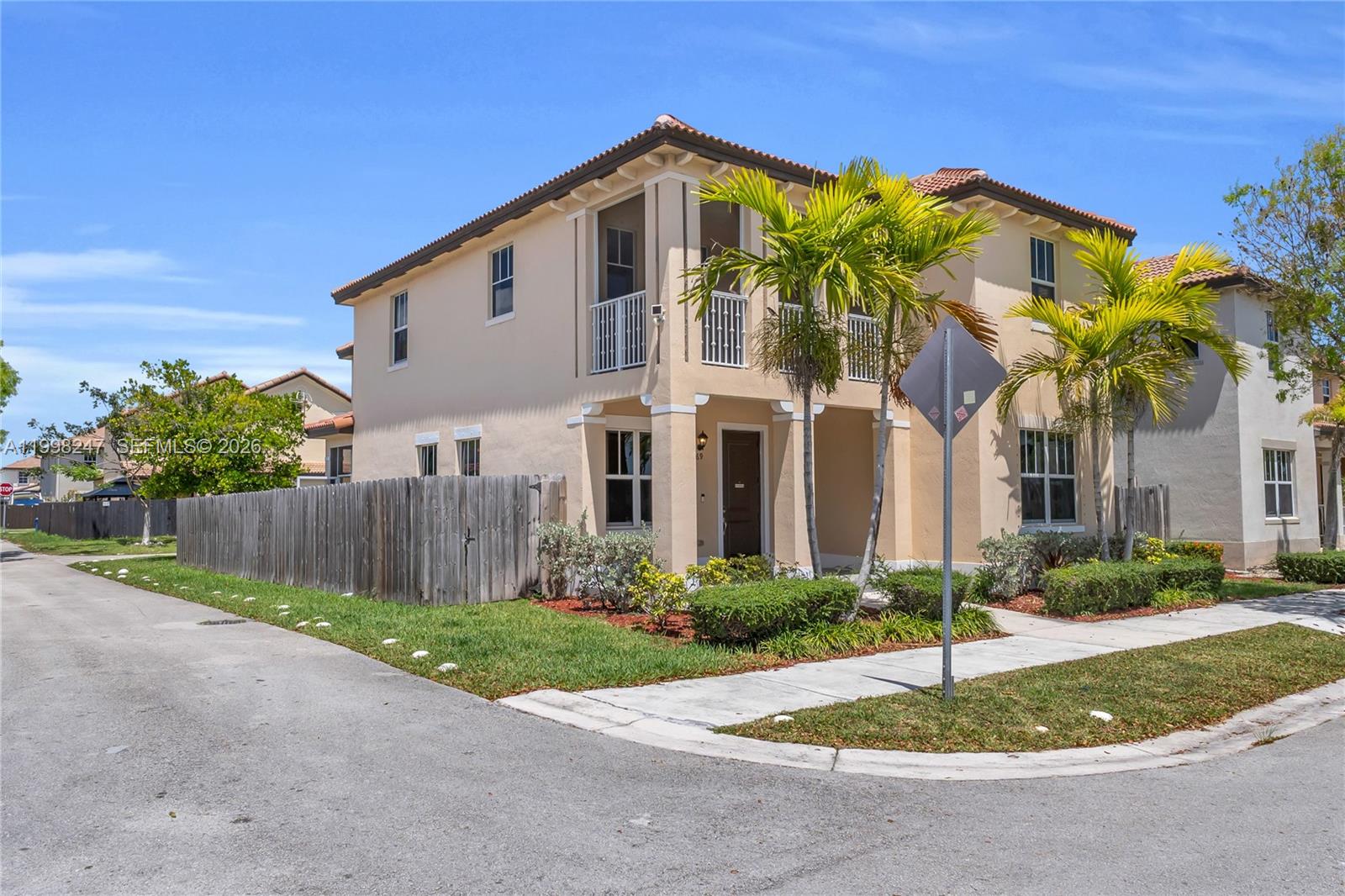 A two-story beige house with a wooden fence and palm trees under a blue sky — 11669 SW 247th St, Homestead FL 33032, HOMESTEAD, FL