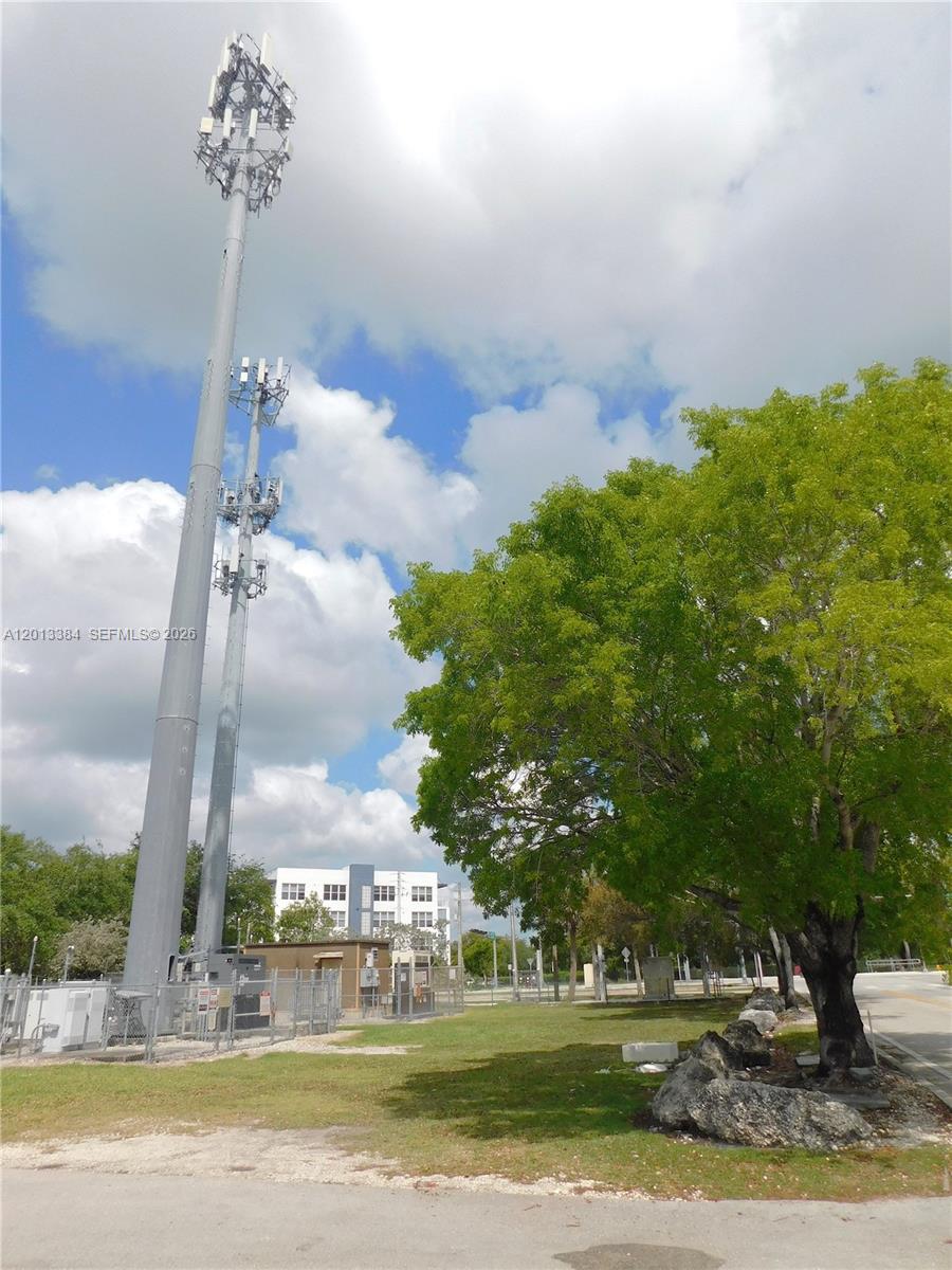 A tall cellular tower stands next to a large tree and a small utility building — 27230 S Dixie Hwy, Homestead FL 33032, HOMESTEAD, FL