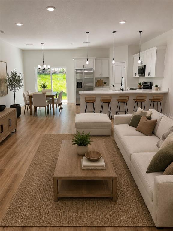 An open-concept living and dining area features light wood floors, white cabinetry, and neutral furniture — 10990 N ADLER DRIVE, DUNNELLON, FL