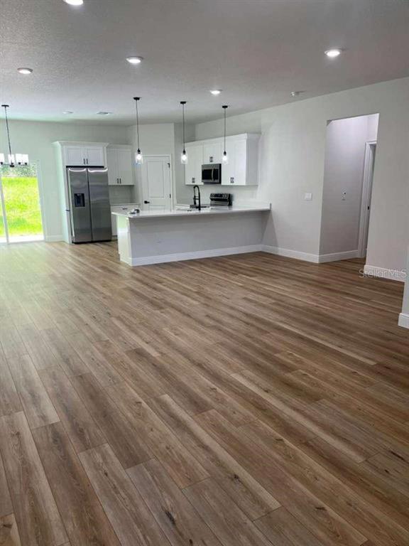 A kitchen with white cabinets, stainless steel appliances, and a breakfast bar overlooks a room — 10990 N ADLER DRIVE, DUNNELLON, FL