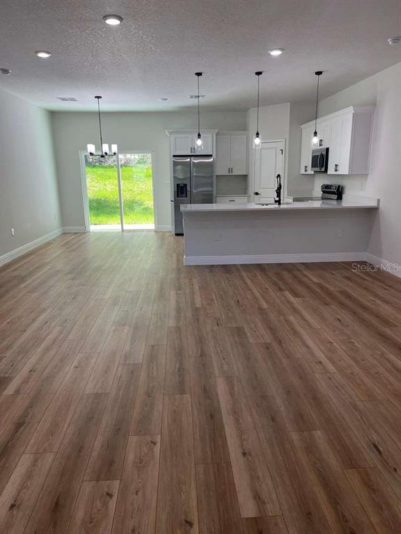 An open-concept kitchen and living area features light wood-look flooring and white cabinetry — 10990 N ADLER DRIVE, DUNNELLON, FL