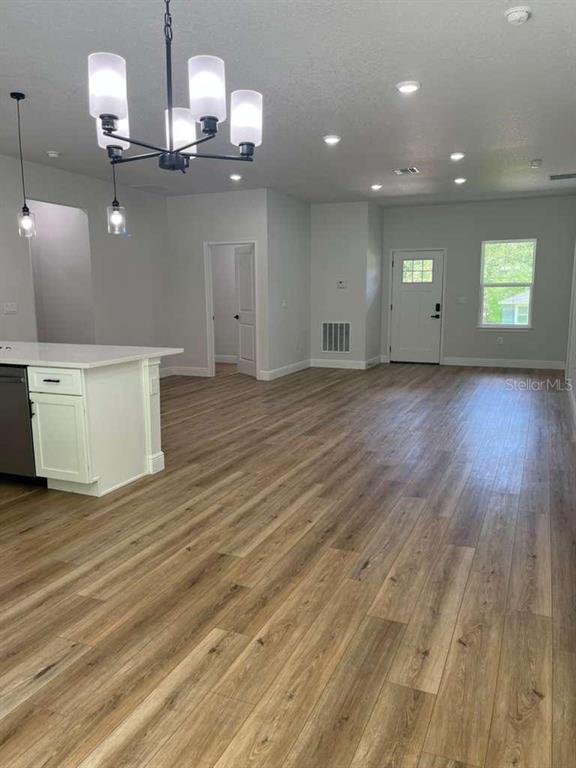 An open-concept kitchen and living area features wood-look flooring, white cabinetry, and a chandelier — 10990 N ADLER DRIVE, DUNNELLON, FL