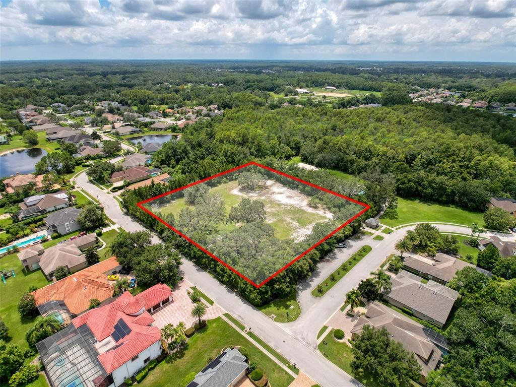 An aerial view shows a vacant, tree-lined lot outlined in red within a residential neighborhood — 15438/15440 AZRA DR, ODESSA, FL