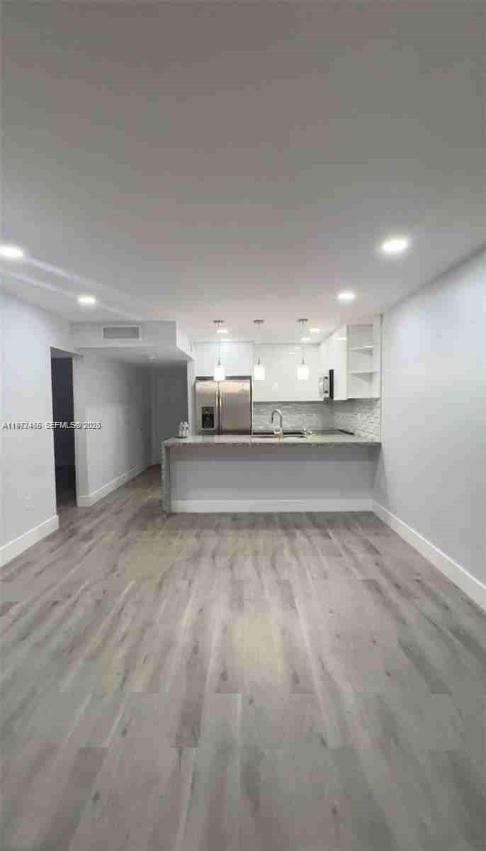 A modern kitchen with white cabinets and a breakfast bar overlooks an open living area — 1555 W 44th Pl # 247, Hialeah FL 33012, HIALEAH, FL