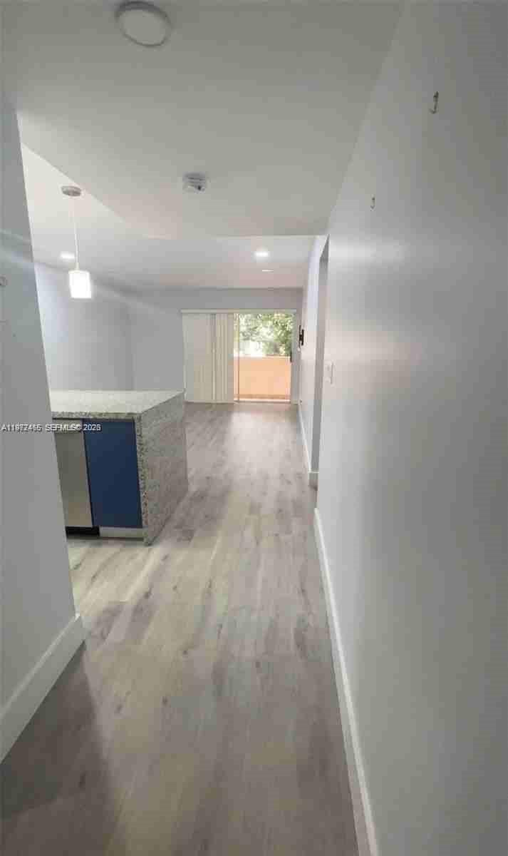 A hallway leads to an open-concept living area with a kitchen island and balcony access — 1555 W 44th Pl # 247, Hialeah FL 33012, HIALEAH, FL