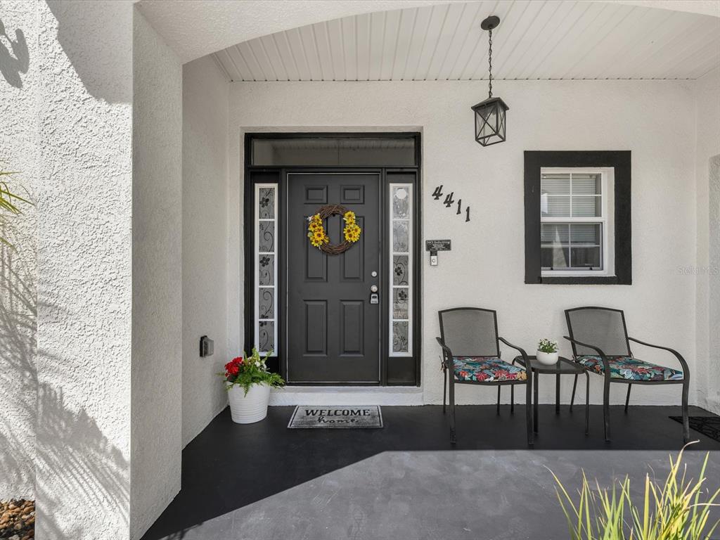 A covered front porch features a black door, two chairs, and a small side table — 4411 W OKLAHOMA AVENUE, TAMPA, FL