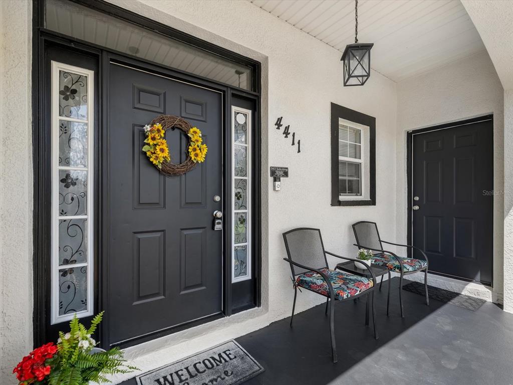 A front porch features two black doors, a sunflower wreath, and two chairs on a mat — 4411 W OKLAHOMA AVENUE, TAMPA, FL