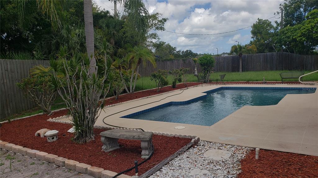 A backyard features a swimming pool, a concrete patio, red mulch landscaping, and a wooden fence — 7223 25TH DRIVE W, BRADENTON, FL