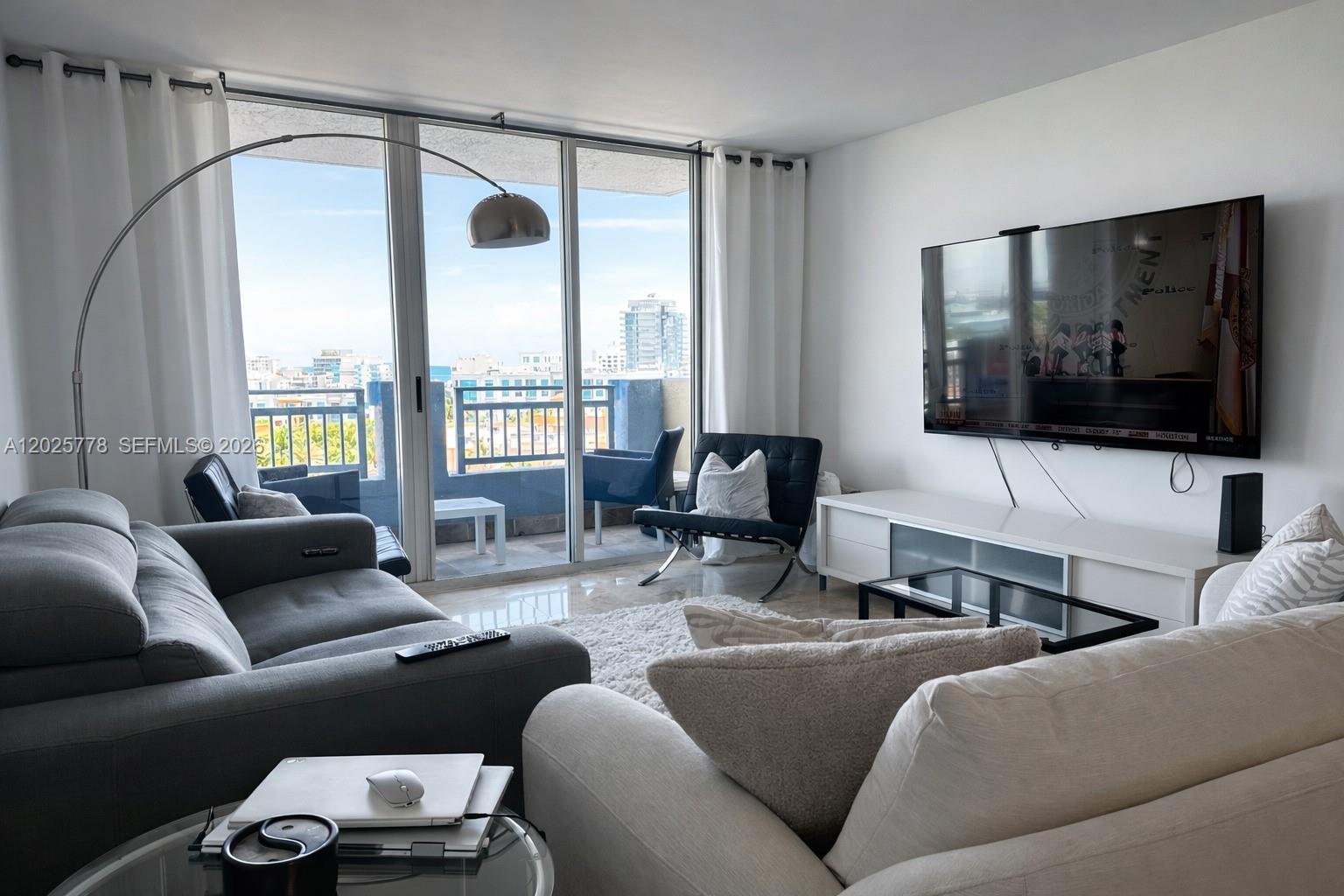A living room features a grey sofa, white couch, television, and a balcony with city views — 90 Alton Rd # 1009, Miami Beach FL 33139, MIAMI BEACH, FL