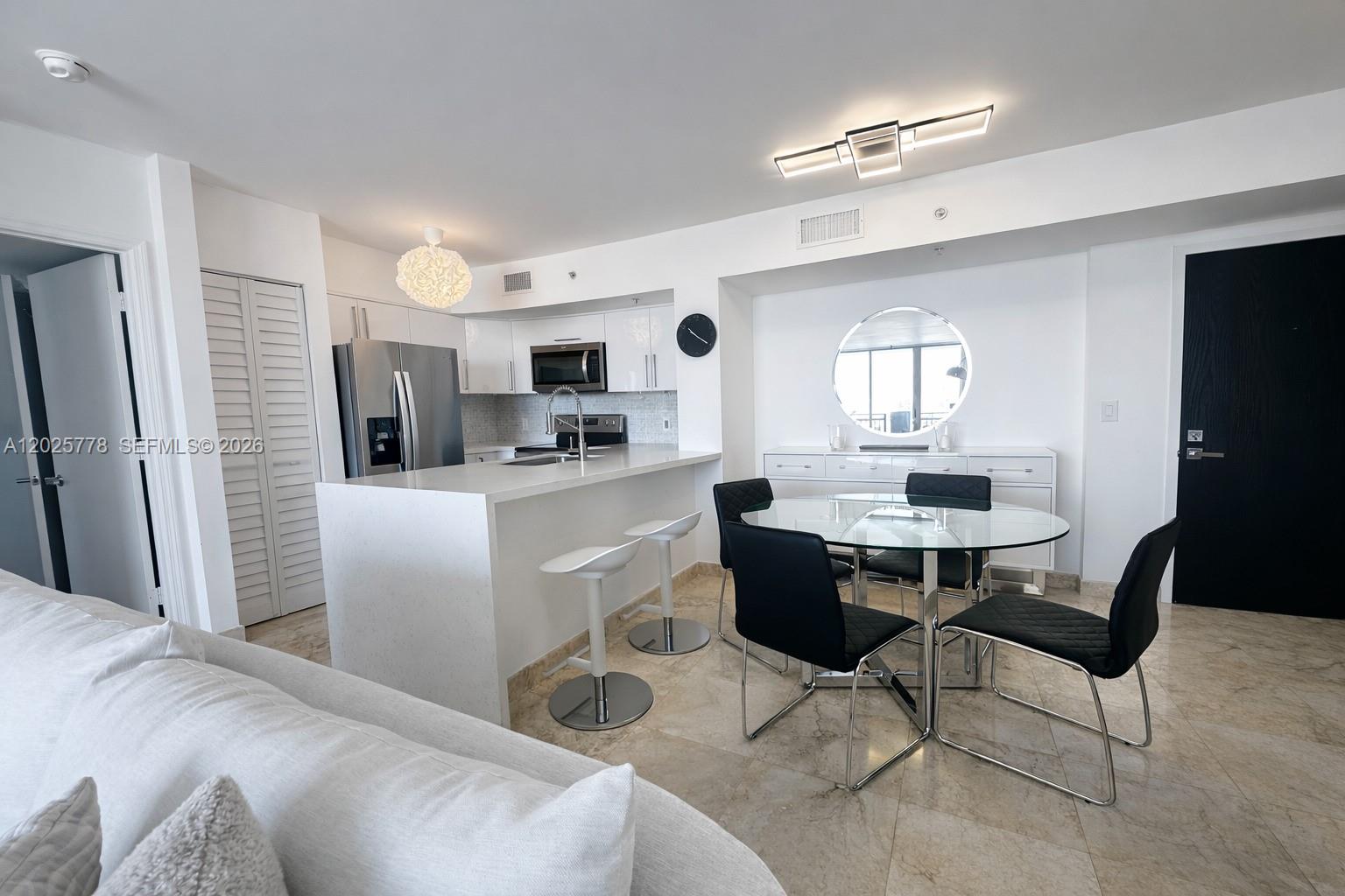 This open-concept kitchen and dining area features white cabinetry, a breakfast bar, and tile flooring — 90 Alton Rd # 1009, Miami Beach FL 33139, MIAMI BEACH, FL