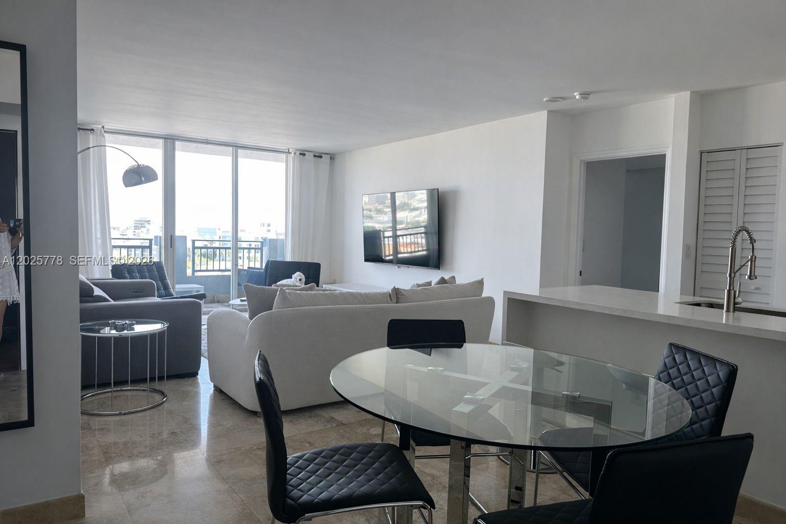 A modern living and dining area features tile floors, a glass table, and balcony access — 90 Alton Rd # 1009, Miami Beach FL 33139, MIAMI BEACH, FL