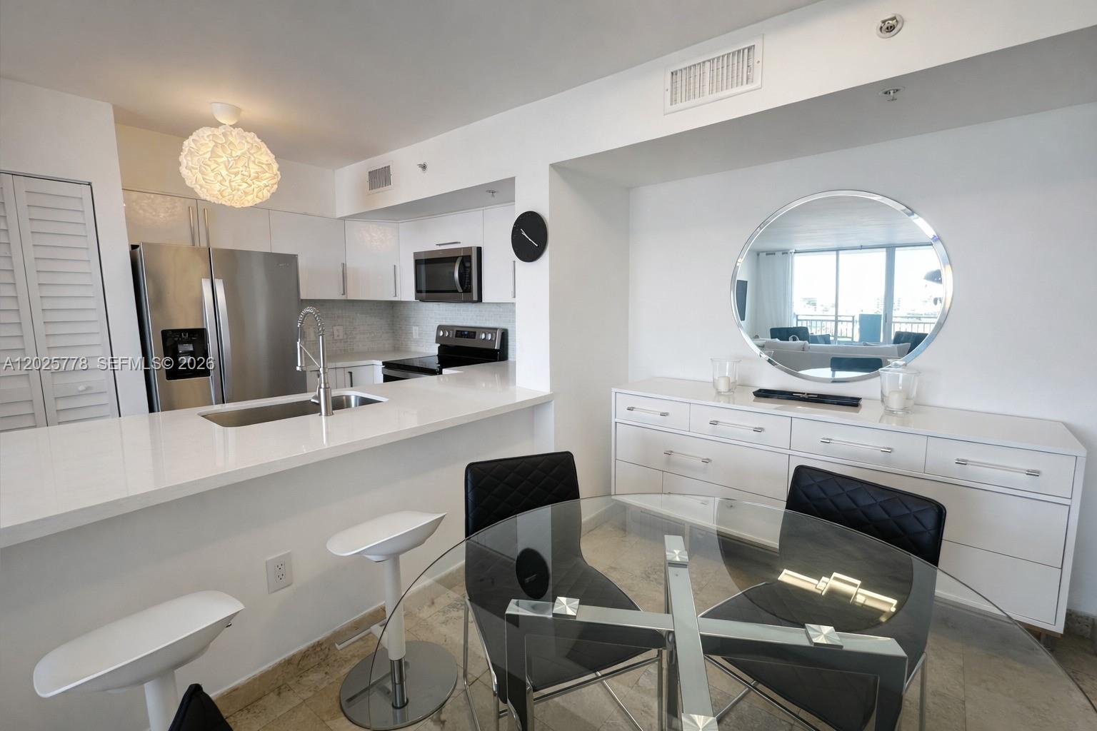 A modern kitchen features white cabinetry, stainless steel appliances, a breakfast bar, and dining area — 90 Alton Rd # 1009, Miami Beach FL 33139, MIAMI BEACH, FL