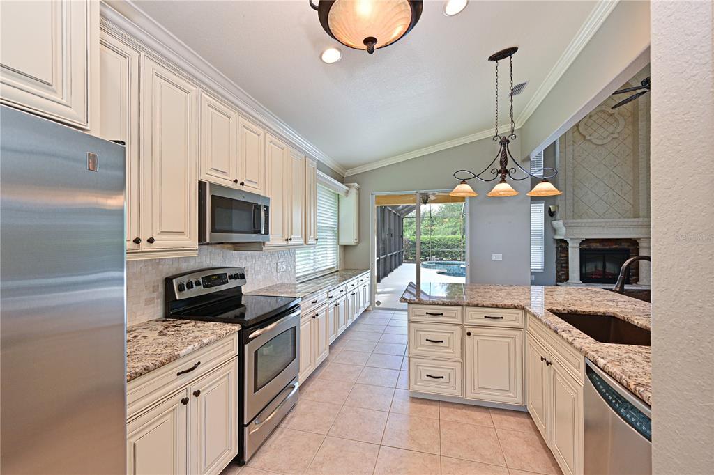 A kitchen with cream cabinets, granite countertops, stainless steel appliances, and a view of a pool — 210 WINDING RIVER TRAIL, BRADENTON, FL